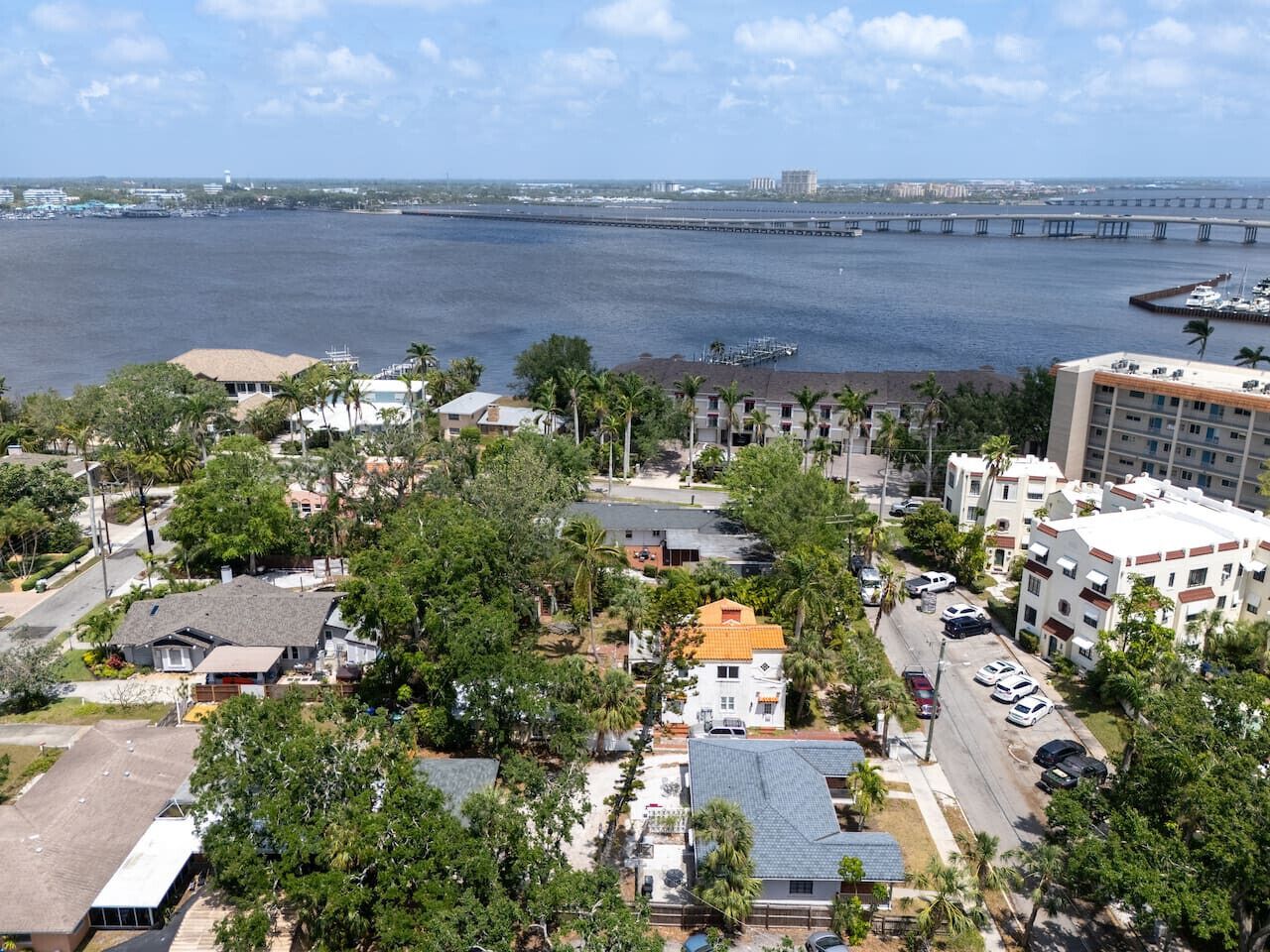 An aerial view of a coastal town with residential buildings, a marina, and a bridge in the background.