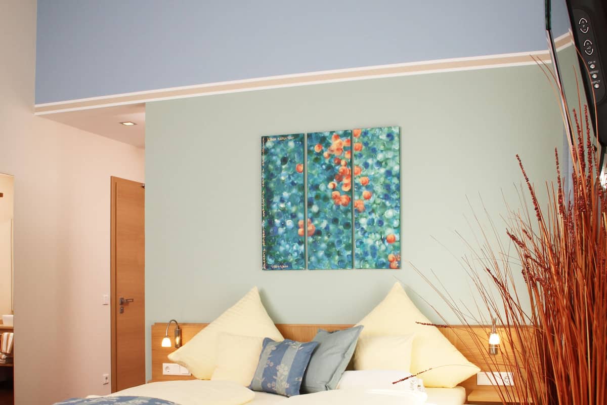 A bedroom with a bed, a nightstand, a wall-mounted TV, and a painting.