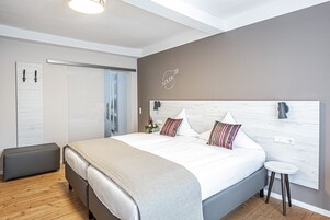 Quarto moderno com uma cama grande, mesa de cabeceira, um banquinho e guarda-roupa.