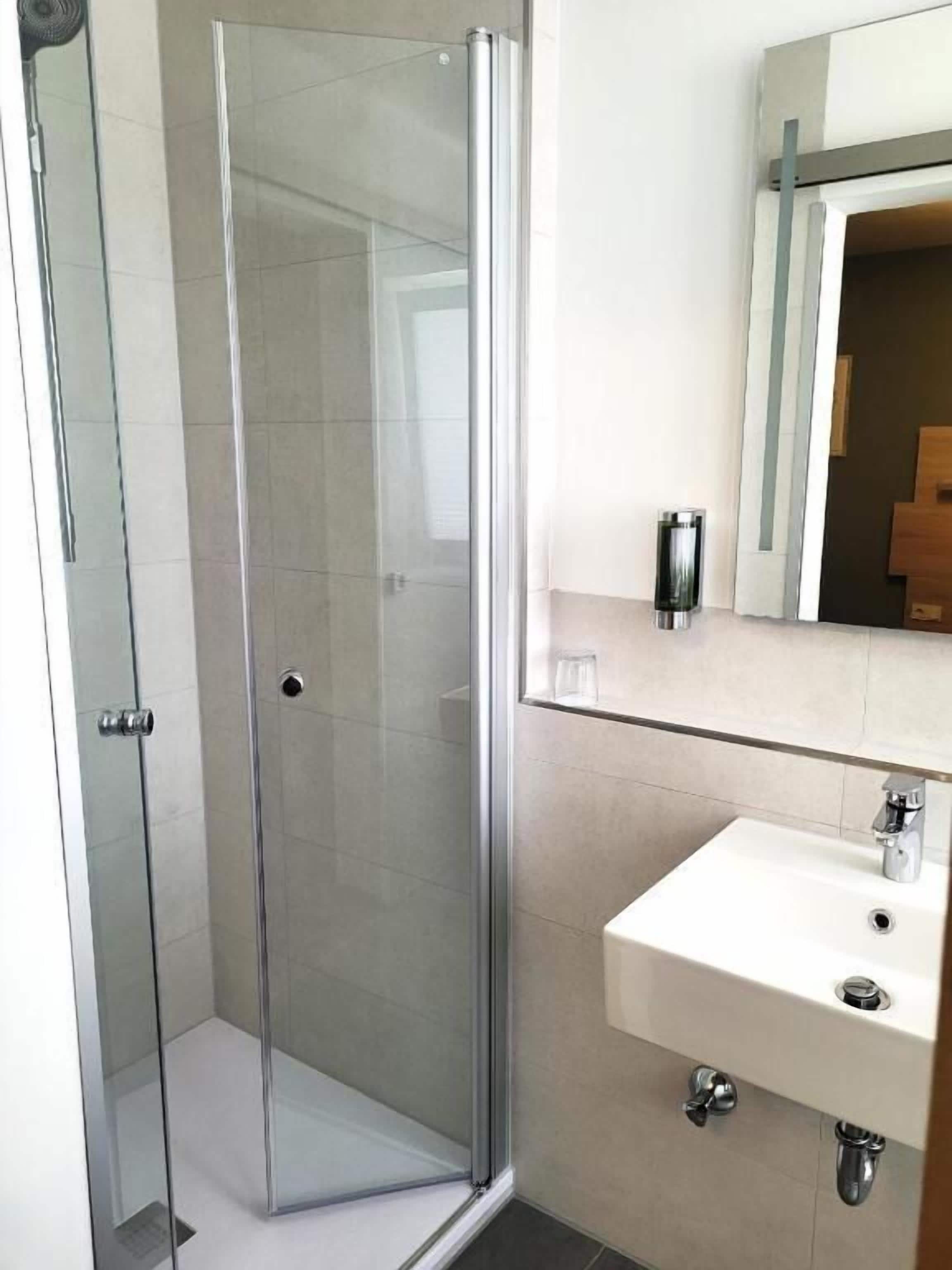A bathroom with a glass-enclosed shower, a white sink, and a mirror above the sink.
