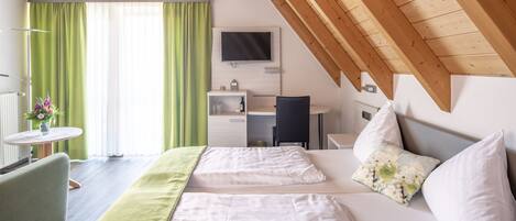 A hotel room with a bed, a desk, a chair, a TV, and a window with curtains.