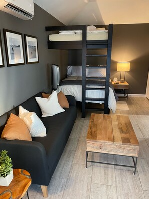 A compact living space with a bunk bed, a sofa, a coffee table, a TV, and framed pictures on the wall.