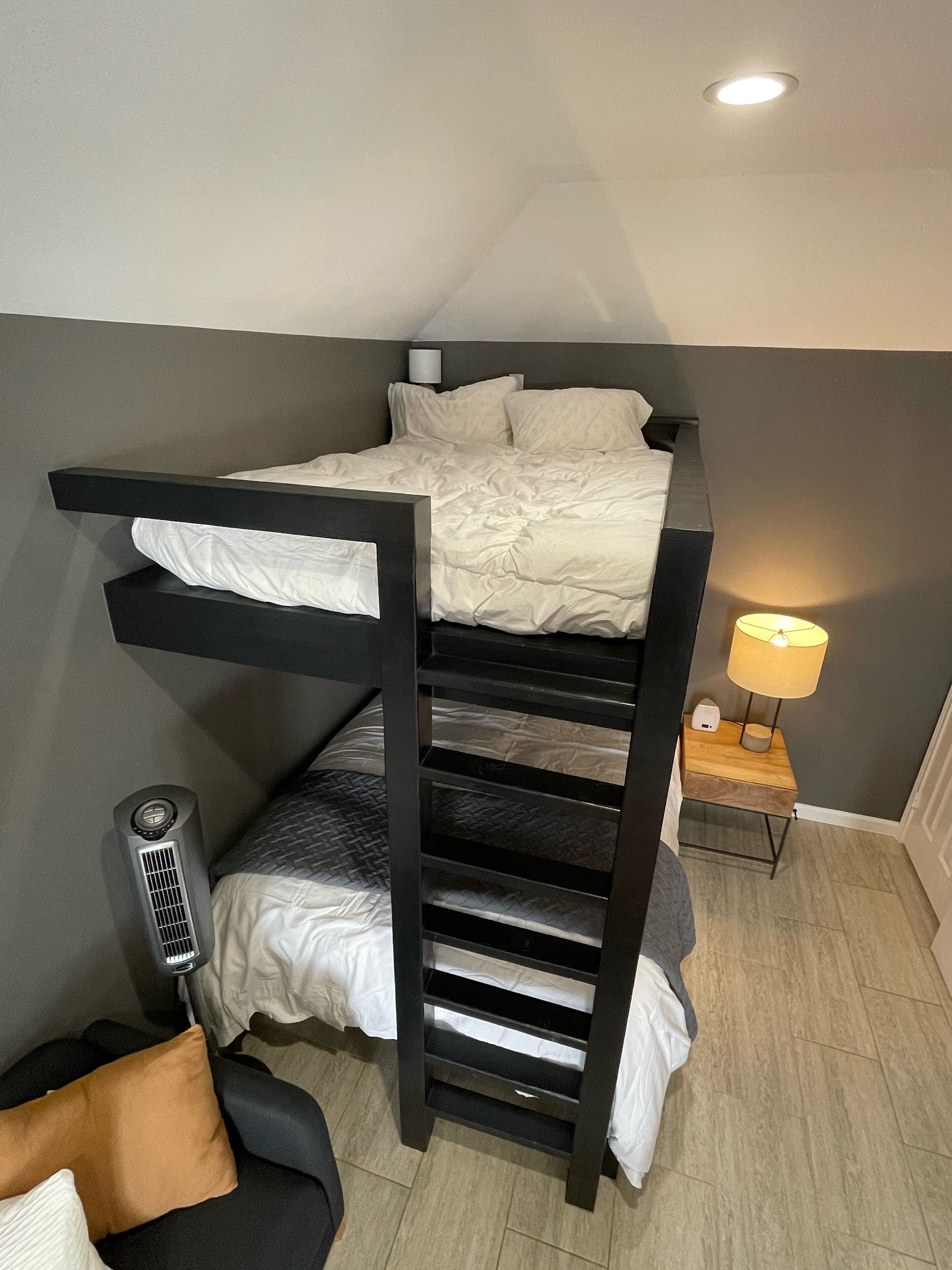Un lit superposé avec un bureau et une chaise, un radiateur mobile et une lampe de chevet.