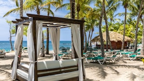 A beach cabana with a thatched roof, surrounded by palm trees and beach chairs.