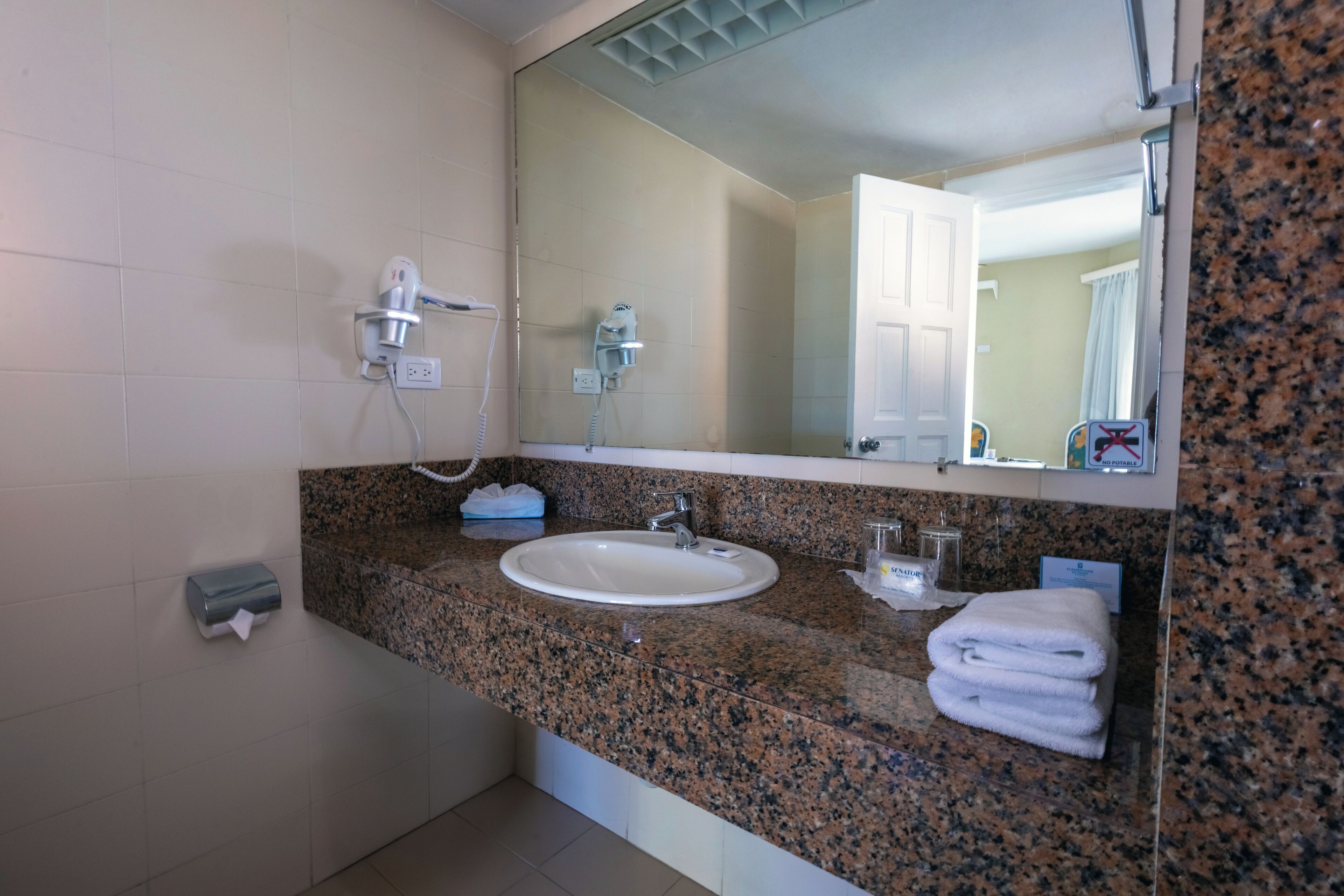 Un baño con encimera de granito, lavamanos, espejo, dispensador de toallas y ducha con cabezal de ducha manual.
