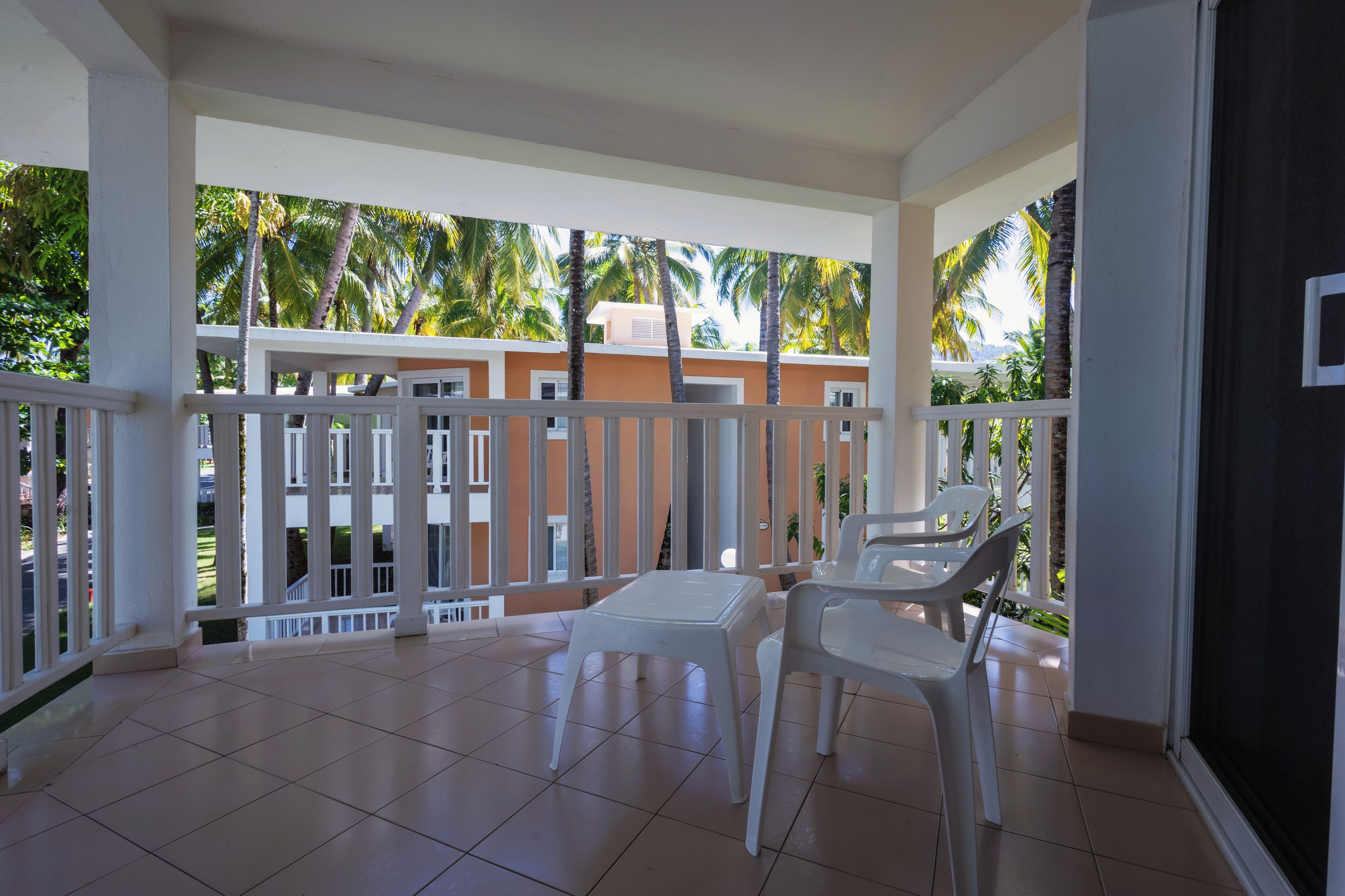 A balcony with white railings, a tiled floor, and two white plastic chairs.