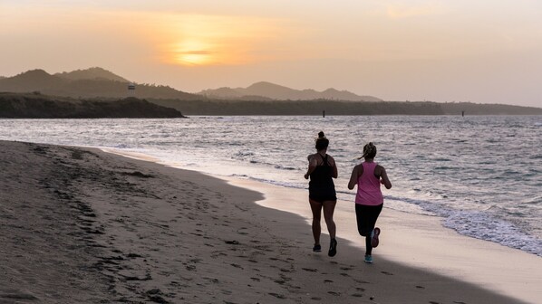 Two people running on a beach with a sunset in the background.