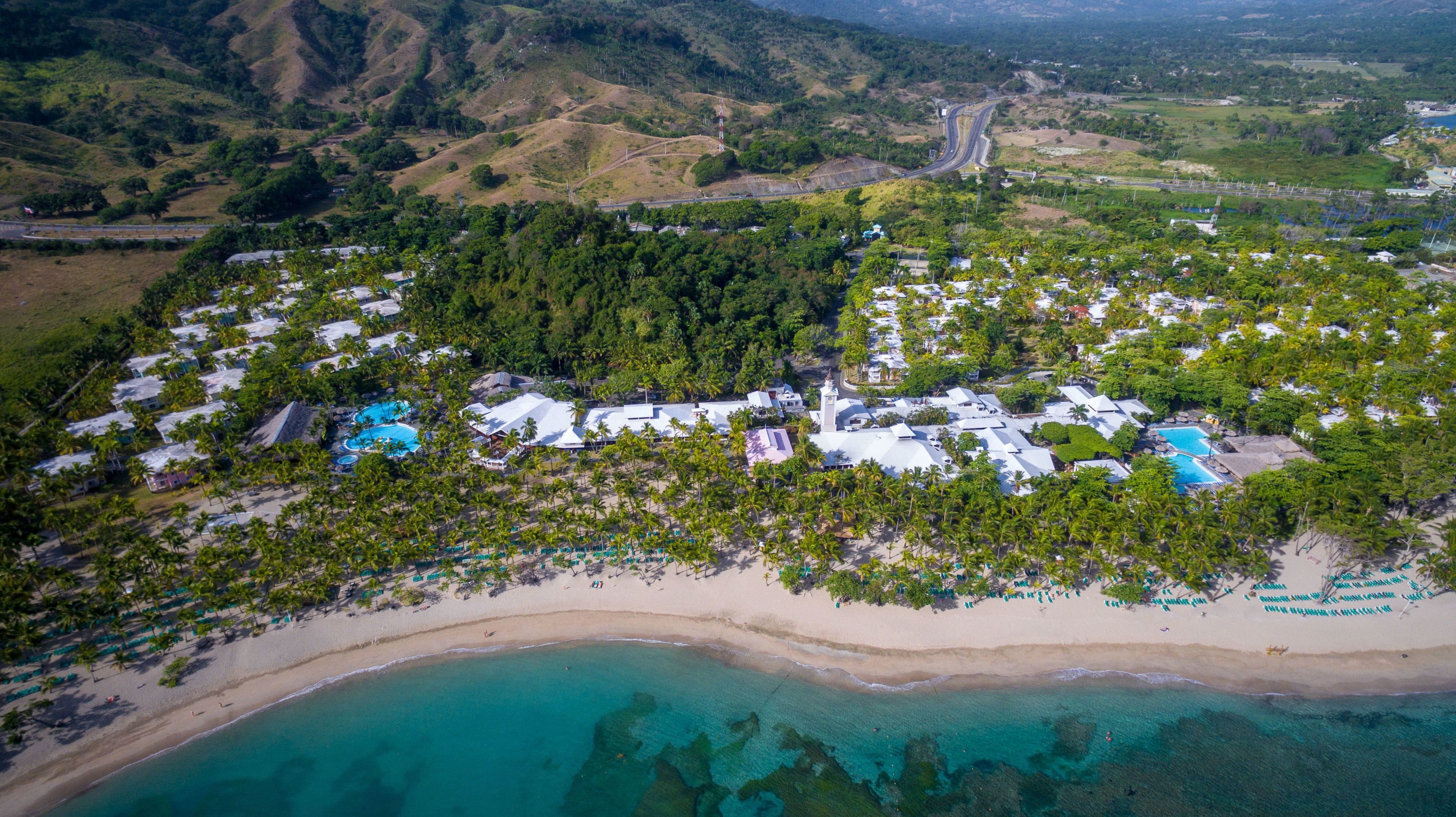 An aerial view of a resort with multiple buildings, a beach, and clear turquoise waters.