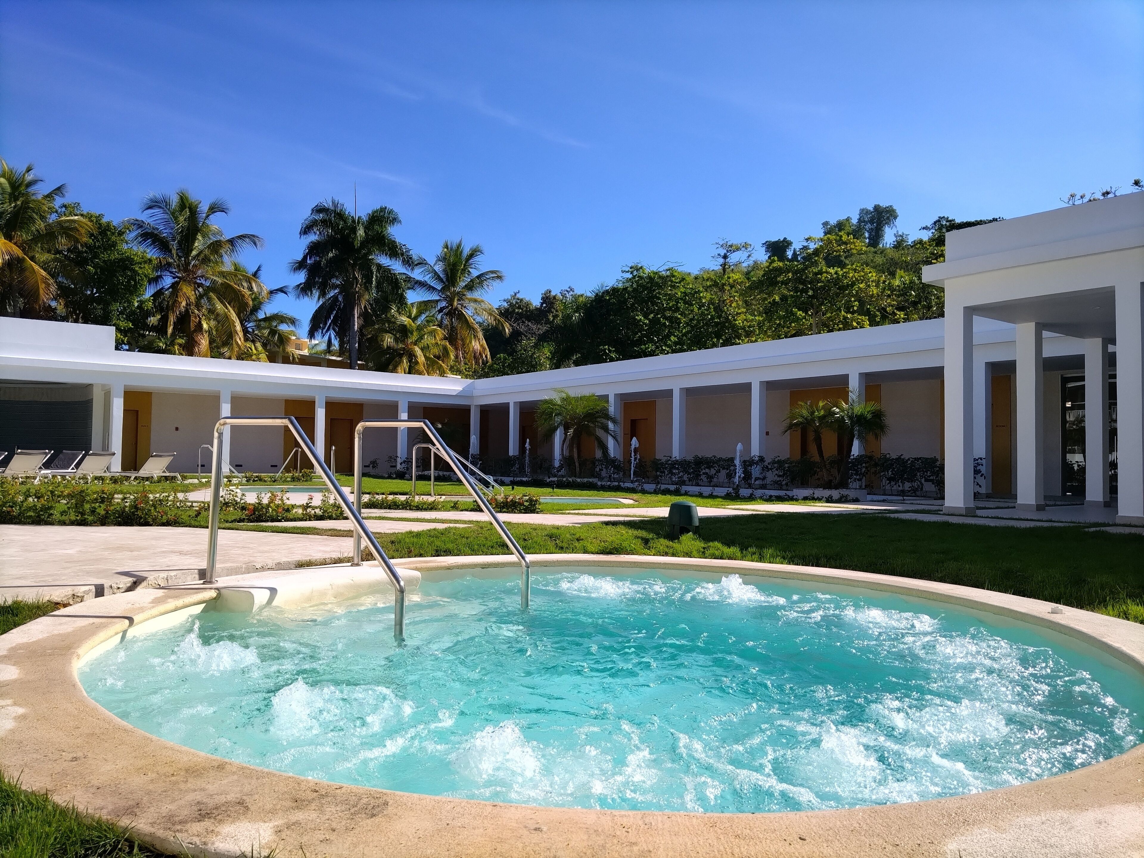 Un espace piscine doté d’un jacuzzi, de chaises longues et d’un coin salon abrité, avec des palmiers en arrière-plan.