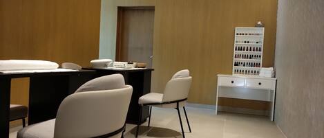 A modern, well-lit room with a reception desk, two chairs, a white console table with a display of nail polish, and a door in the background.