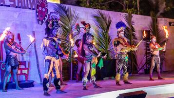 Un escenario con artistas vestidos con trajes tradicionales, sosteniendo antorchas, y un cartel que dice 'A SHOWY'.