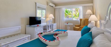 A hotel room with a bed, a TV, a desk, a chair, and a window with a view of palm trees.