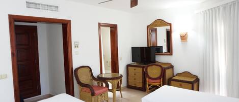A hotel room with two beds, a television, a desk with a chair, a ceiling fan, and a large mirror.