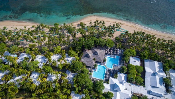 An aerial view of a resort with multiple swimming pools, a beach, and lush greenery.