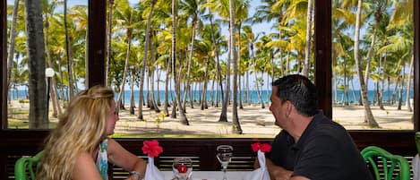 A couple dining at a table with a view of a beach and palm trees.