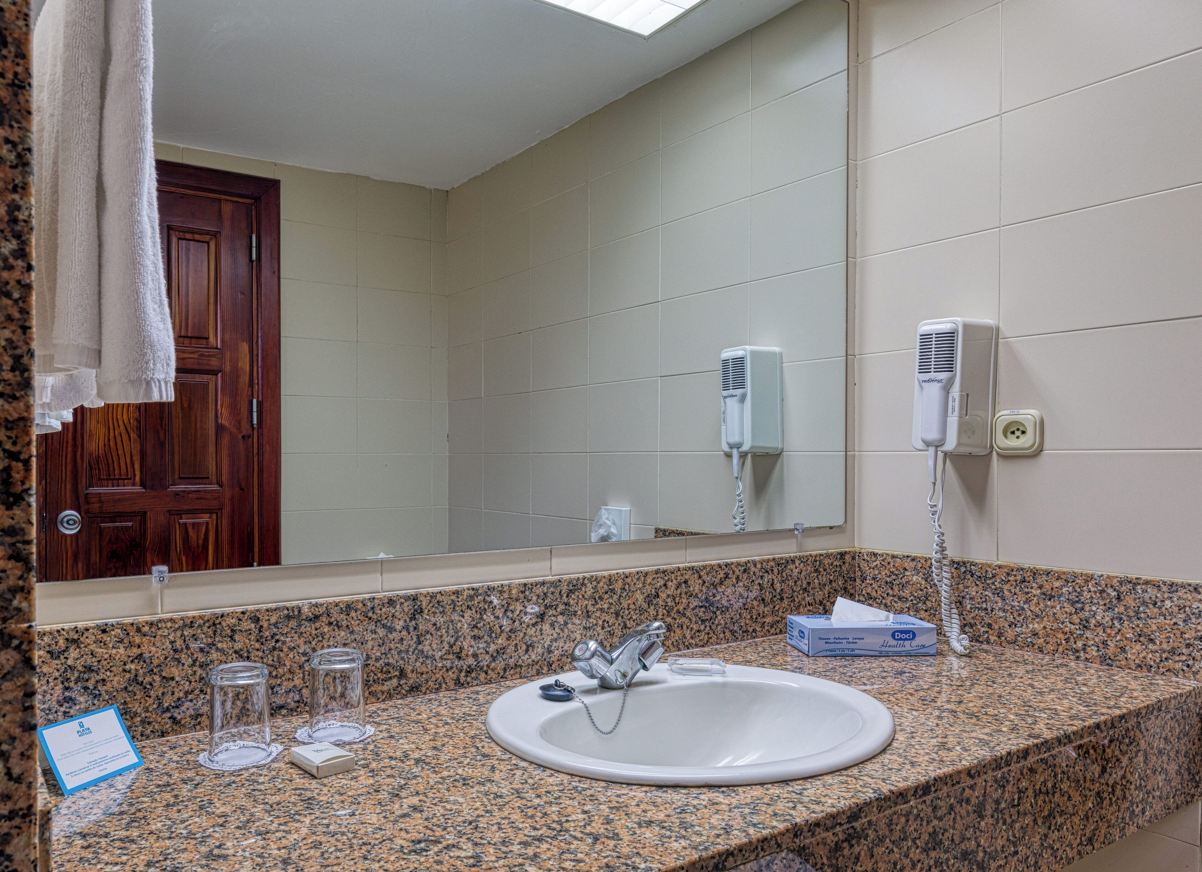 A bathroom with a granite countertop, a sink, a mirror, a hairdryer, and a towel rack.