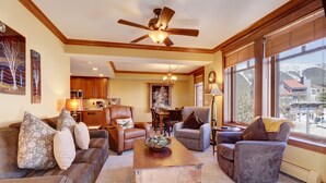 A spacious living room with a ceiling fan, a wooden coffee table, leather sofas, and a view of the mountains through large windows.