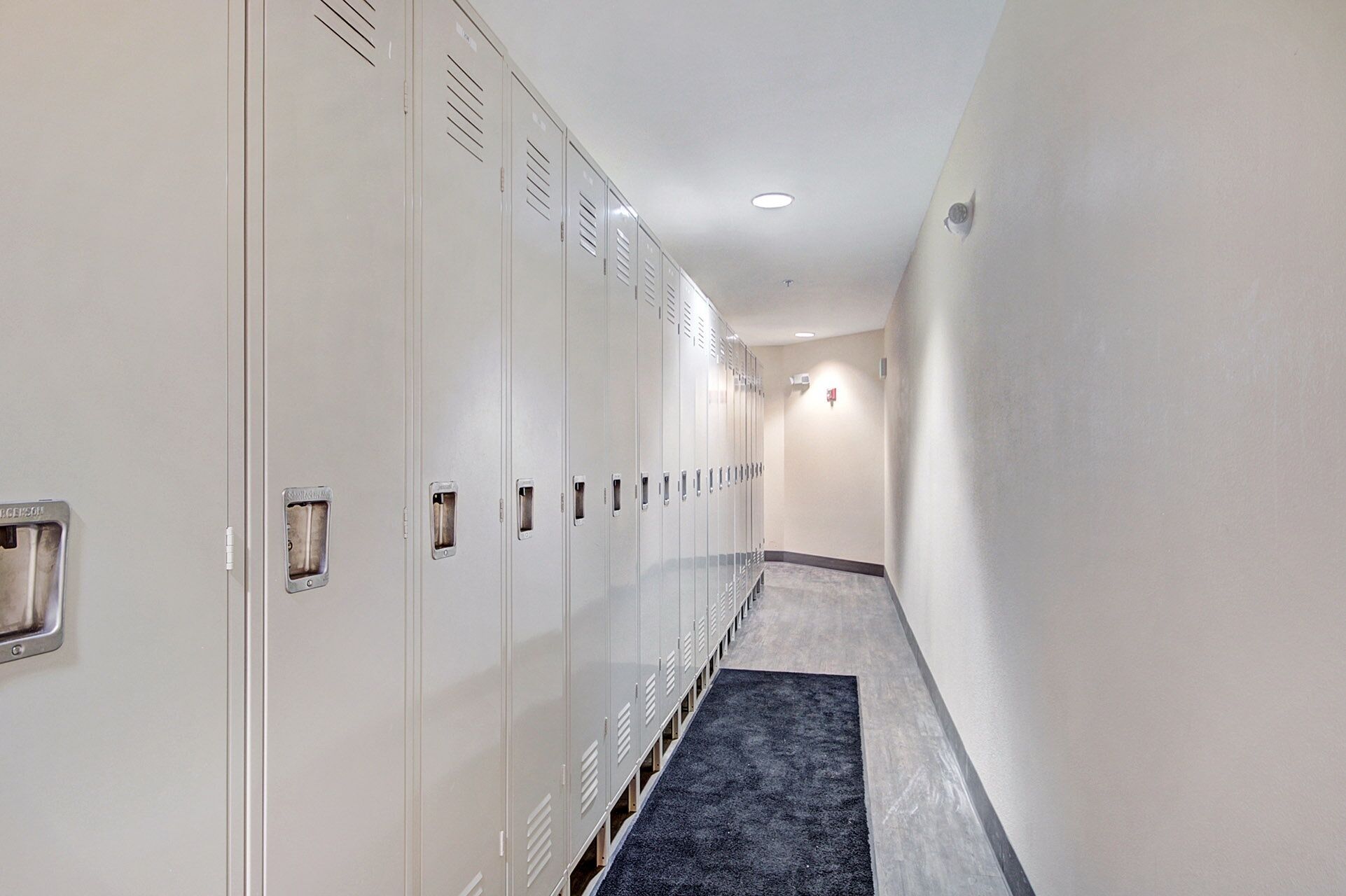A hallway with lockers, a carpeted floor, and a light fixture on the ceiling.