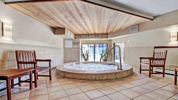 A spa area with a hot tub, wooden chairs, and a tiled floor.