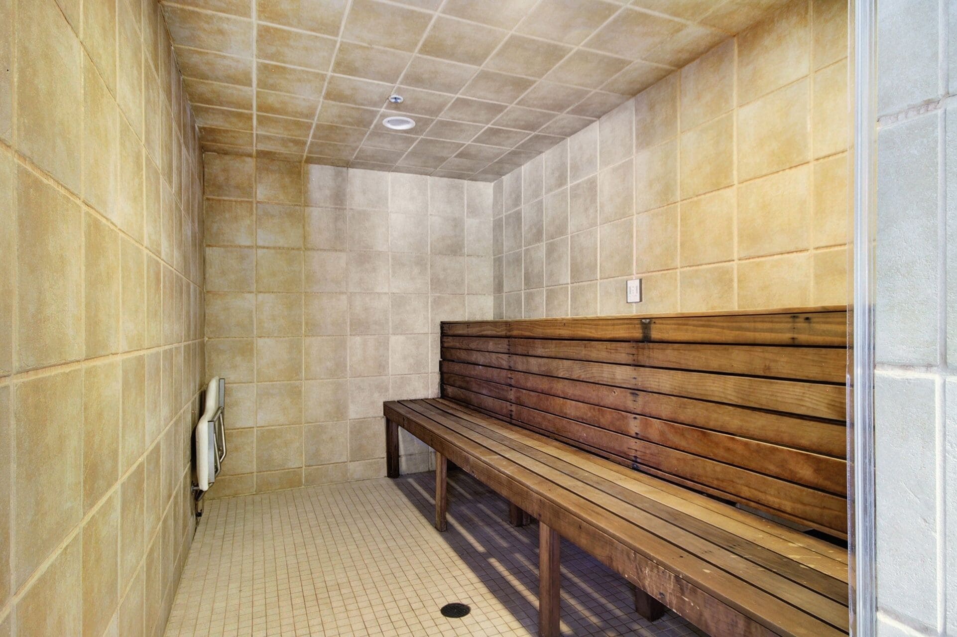 Eine Sauna mit Kacheln, einer Holzbank und einem Lüftungssystem.