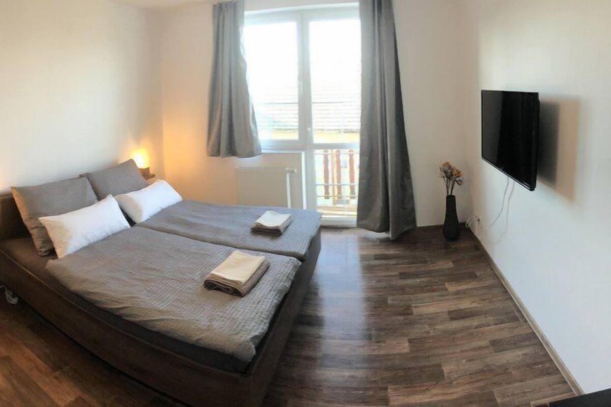 A bedroom with a double bed, bedside tables, a dresser, a TV, and a window with curtains.