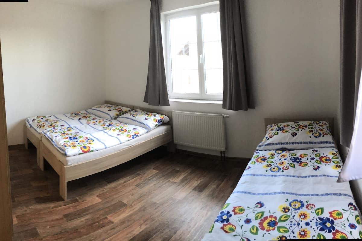 A small, well-lit room with two single beds, a radiator, and a window with curtains.