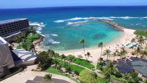 A beach resort with a view of the ocean, palm trees, and a building with solar panels.