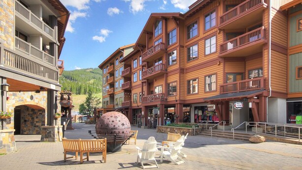 Un edificio de madera de varios pisos con balcones, una entrada con arco de piedra y mobiliario exterior.