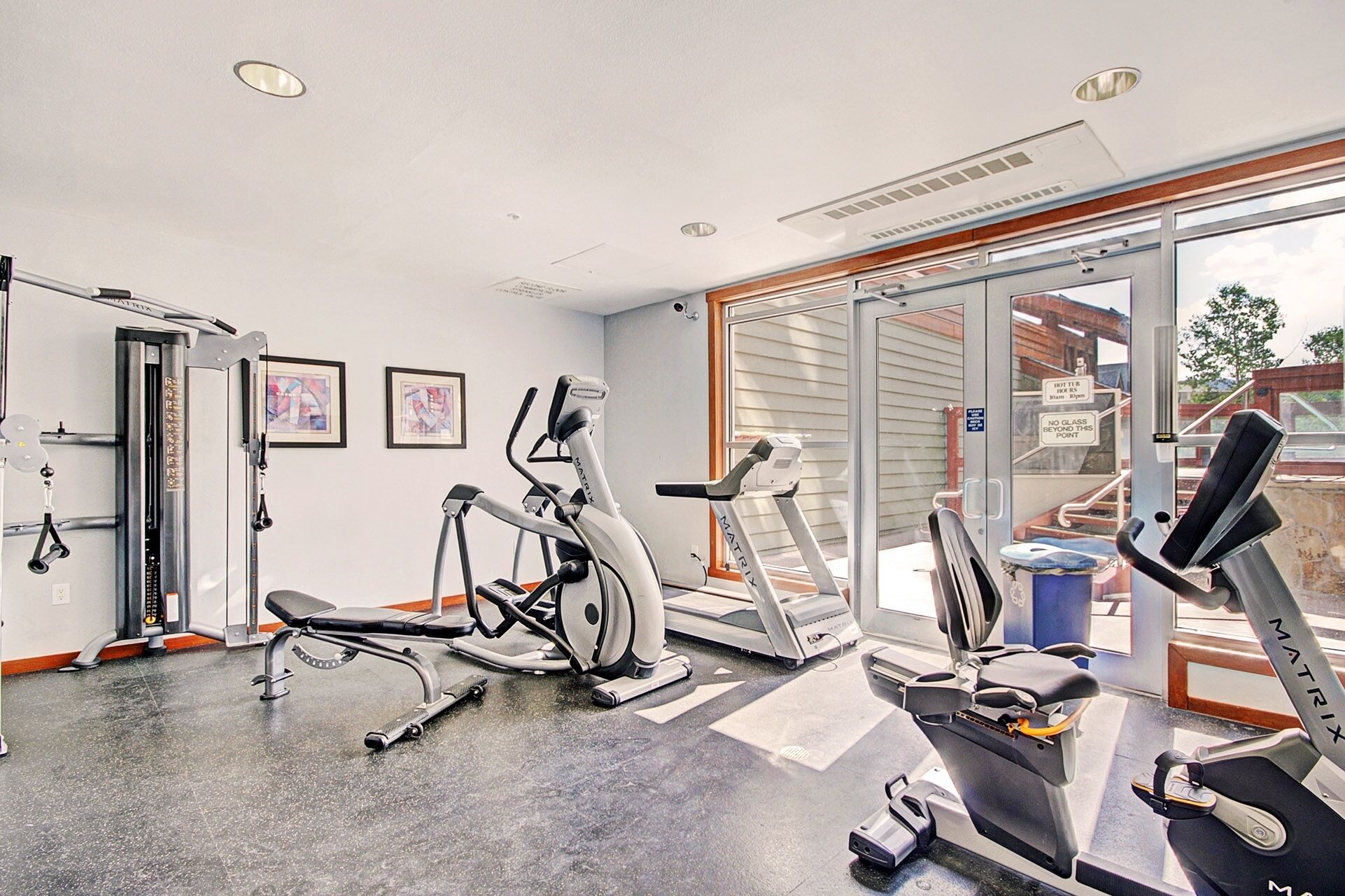 A gym with cardio machines, weight training equipment, and a large window providing a view of the outside.
