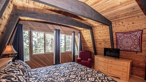 Une chambre à coucher avec un lit, une commode, un téléviseur et une fenêtre avec des rideaux.