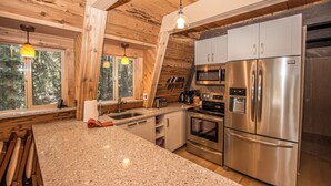 Une cuisine dotée de plans de travail en granit, d’appareils électroménagers en acier inoxydable et de poutres en bois.