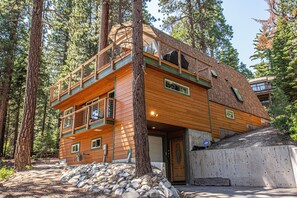 Une cabane en bois à plusieurs niveaux, dotée d’un balcon et entourée d’arbres.