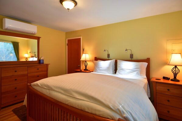 A neatly made bed in a hotel room with a wooden headboard, two bedside tables with lamps, a mirror above the dresser, and an air conditioning unit on the wall. - SUNNY & SPACIOUS 2BD CONDO - AC - GAS FIREPLACE - 5 STAR RATINGS (Seattle)