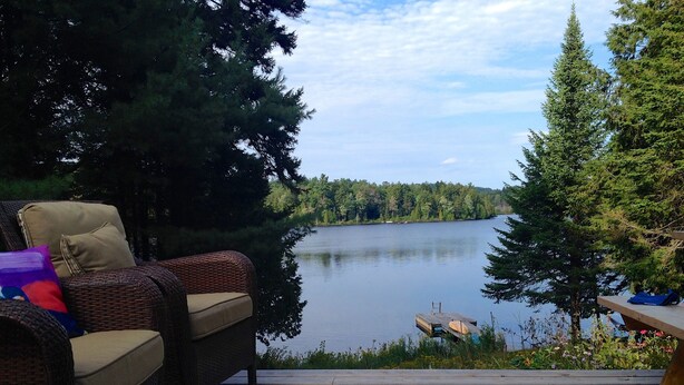 A wooden deck with wicker furniture and a view of a lake surrounded by trees. - Beautiful lakefront cottage, 1 hour north of Montreal (Wentworth)