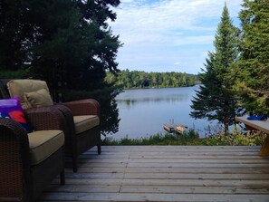 A wooden deck with wicker furniture and a view of a lake surrounded by trees. - Beautiful lakefront cottage, 1 hour north of Montreal (Wentworth)