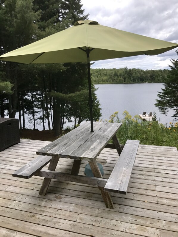 En träveranda med ett picknickbord och ett grönt parasoll.