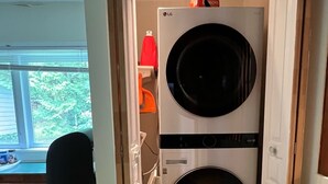 A laundry room with a double washer and dryer, wooden beams on the ceiling, a window with blinds, and a blue recycling bin. - Beautiful lakefront cottage, 1 hour north of Montreal (Wentworth)