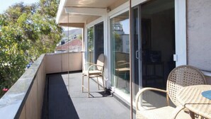 Un balcon avec deux fauteuils en osier, une petite table et une porte-fenêtre coulissante donnant sur un espace intérieur.