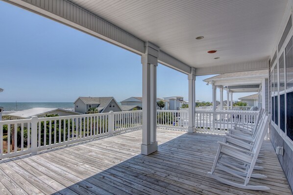 A wooden deck with white railings overlooking a beach.