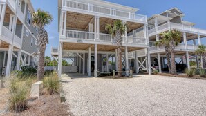 Une propriété en bord de mer, composée de plusieurs étages, dotée de balcons, d’un porche couvert et d’une allée en gravier.