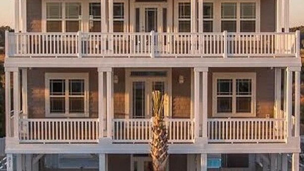 Un immeuble de deux étages, doté d’un balcon à chaque étage, d’une entrée couverte et d’un palmier au premier plan.