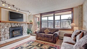 Ein Wohnzimmer mit Kamin aus Stein, Ledersofas, einem Flachbildfernseher und einem großen Fenster mit Blick auf die Stadt.