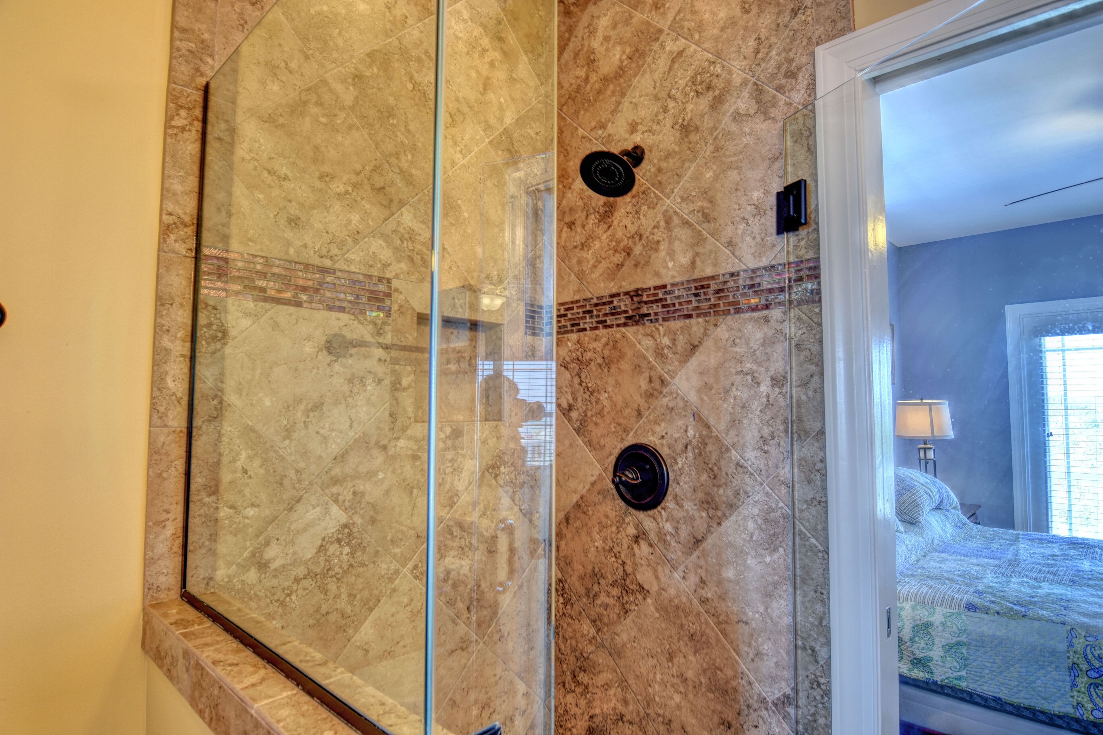Une salle de bain dotée d’une douche à parois de verre, de murs en marbre et d’un lit visible dans la pièce adjacente.