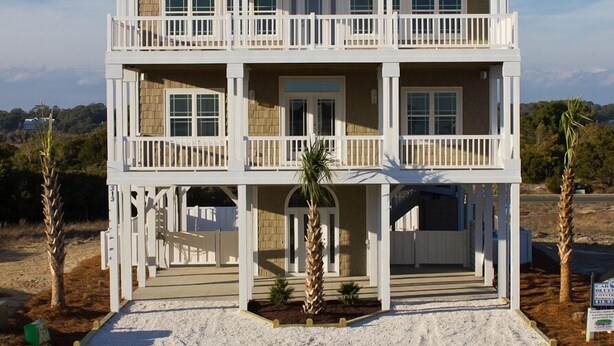 A two-story beachfront house with a balcony on each floor, a covered front porch, and a sandy driveway. - Luxury 5BR · Sleeps 17 · 1st St  · 50 Yards to Beach · Pool · Elevator (Ocean Isle Beach)