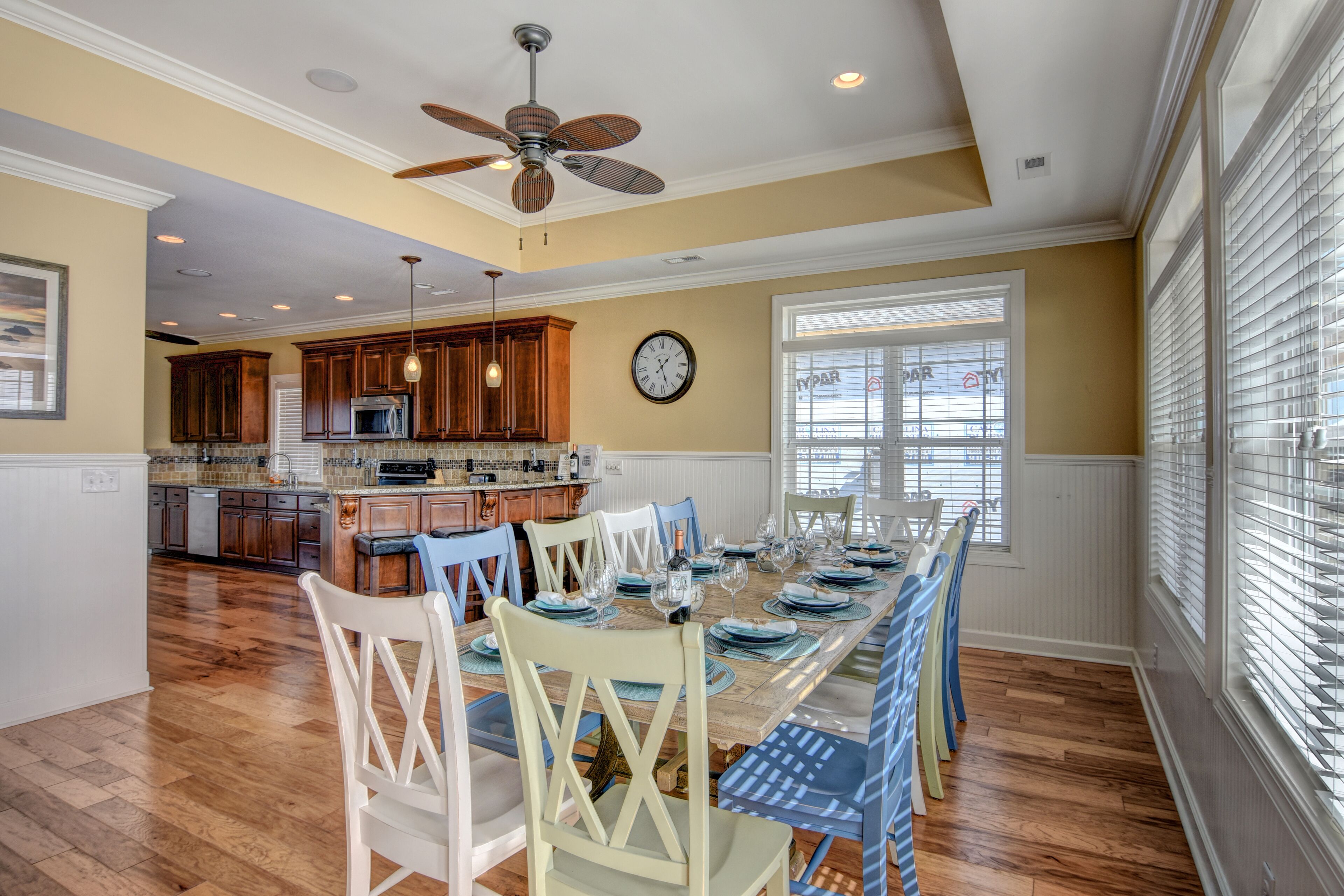 A spacious kitchen with wooden cabinets, a dining area with a long table set for six, and a ceiling fan.