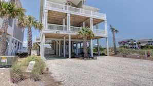 A two-story beachfront house with a covered porch, palm trees, and a gravel driveway. - Luxury 5BR · Sleeps 17 · 1st St · 50 Yards to Beach · Pool · Elevator (Ocean Isle Beach)