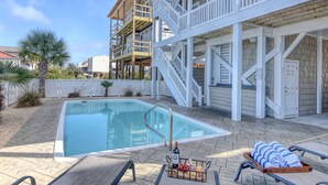 A pool area with a clear pool, a wooden deck, and a white building with a balcony. - Luxury 5BR · Sleeps 17 · 1st St · 50 Yards to Beach · Pool · Elevator (Ocean Isle Beach)