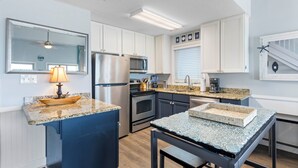 Een moderne keuken met witte kasten, roestvrijstalen apparatuur, een granieten aanrechtblad en een blauw eiland.