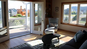 Ein geräumiges Wohnzimmer mit einer großen Glasschiebetür, die auf einen Balkon führt, einem bequemen Sofa und einem Sessel mit Blick auf die Nachbarschaft.