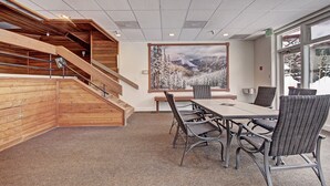 A conference room with a large table and chairs, a staircase with wooden railings, and a large window with a mountain view. - Spacious Condo in the Heart of Center Village - Pet Friendly - VS367 by Redawning (Copper Mountain)